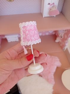 a hand holding a miniature lamp in a doll's house with furniture and accessories