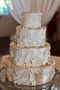 a three tiered wedding cake with white flowers on the top and bottom, sitting on a silver platter