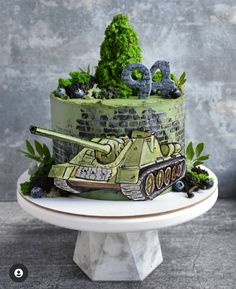 a birthday cake decorated with an army tank and trees on the top, surrounded by greenery