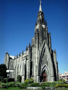 an old church with a steeple and clock on it's side, surrounded by greenery