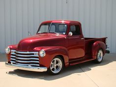 an old red pickup truck parked in front of a garage door with the words classic & vintage cars & hot rods written on it