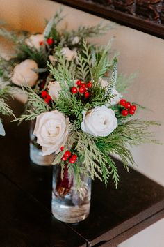 two vases filled with flowers and greenery on top of a wooden table next to a mirror