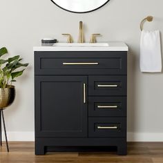 a white sink sitting under a round mirror next to a black cabinet with gold handles