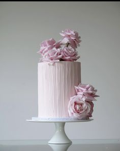 two tiered cake with pink icing and flowers on the top, sitting on a white pedestal