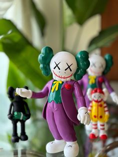 three toy clowns are standing on a glass table next to a potted plant