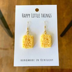 a pair of yellow earrings sitting on top of a white piece of paper with the words happy little things written in it