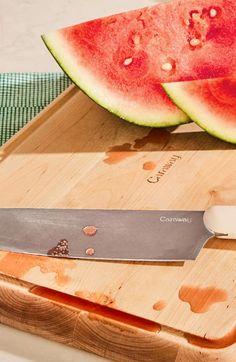 a watermelon cut in half on a cutting board with a knife