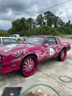 the pink car has been painted with flowers on it's side and is parked next to other cars