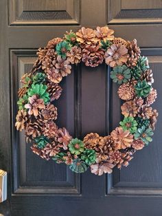 a wreath made out of pine cones and green leaves on a front door with a candle