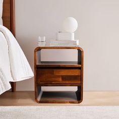 a night stand with two drawers and a lamp on it next to a white bed