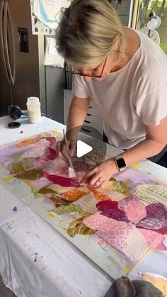 a woman is painting on a large piece of paper with watercolors and ink