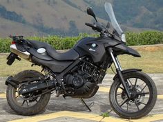 a black motorcycle parked on top of a parking lot next to a lush green hillside