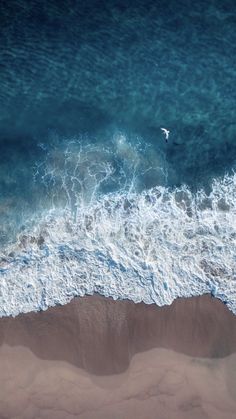 an aerial view of the ocean and beach with waves crashing on it's shore