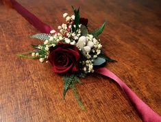 a boutonniere with flowers and greenery on a wooden table in front of a red ribbon