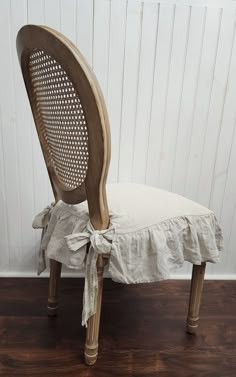 a wooden chair with a white ruffled seat and back cover sitting on a hard wood floor