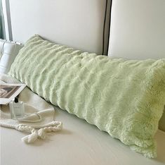 a green pillow sitting on top of a bed next to a phone and other items