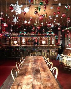 a long wooden table sitting in front of a bar with christmas decorations hanging from the ceiling