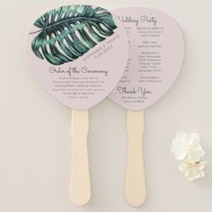 two fans with palm leaves on them next to a white flower and a small piece of paper