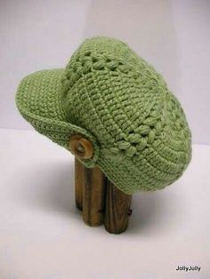 a green crocheted hat sitting on top of a wooden stand with a button