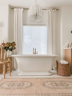 a white bath tub sitting under a chandelier in a bathroom next to a window