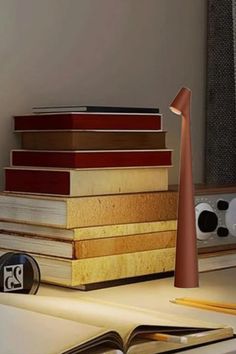 A cozy desk scene with a stack of books and a sleek table lamp casting warm light. Nearby are pencils, a clock, and flowers, creating a peaceful ambiance.