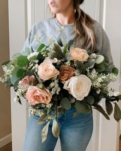 a woman standing in front of a door holding a bouquet of roses and greenery