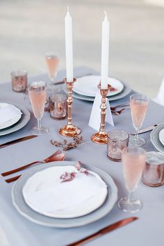 the table is set with silver and white plates, wine glasses, candles, and napkins