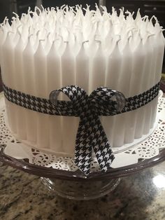 a cake with white frosting and black ribbon on a glass platter sitting on a table