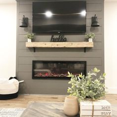 a living room with a tv mounted above the fireplace and two potted plants in front of it