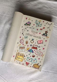 an open book with drawings on it sitting on top of a white bed sheet that says love other words