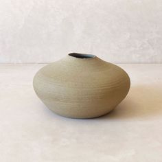 a small white vase sitting on top of a table next to a gray and white wall