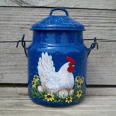 a painted chicken on a blue pot with yellow daisies and daisies around it