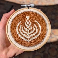 a person holding up a brown and white embroidered object with leaves on it's side