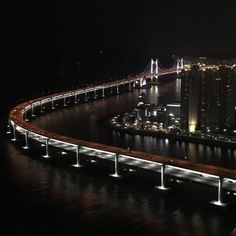 an aerial view of a city at night with lights on the road and bridge in the background