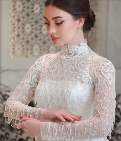 the woman is wearing a white dress with long sleeves and an intricate lace pattern on it