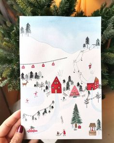 a person holding up a card with a drawing of a snowy village and trees on it