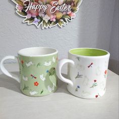 two coffee mugs sitting next to each other on a white table with a happy easter sign in the background