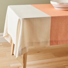 an orange and white table cloth on top of a wooden table with a bowl in the background