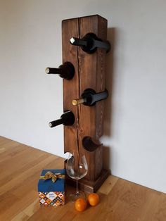 a wooden wine rack holding several bottles and two glasses next to an orange on the floor