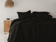 a bed with black linens and pillows in a white room next to a plant