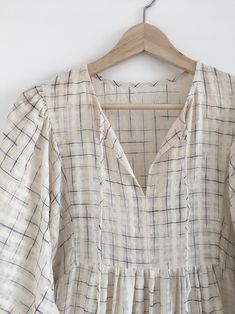 a white shirt with blue and black lines on it hanging from a wooden hanger