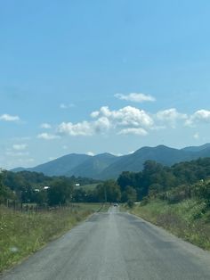 an empty road with mountains in the background and grass on both sides, under a blue cloudy sky