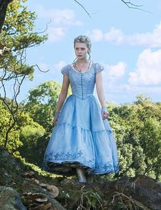 a woman in a blue dress standing on top of a tree branch with her hands behind her back