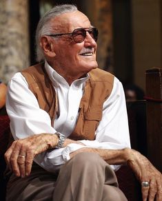 an older man sitting on top of a red couch next to a woman in white shirt and tan pants