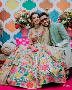 a man and woman sitting next to each other in front of a wall with flowers