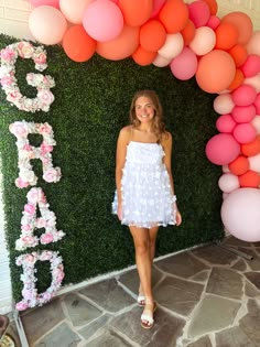 a young woman standing in front of a backdrop with balloons and flowers on the wall