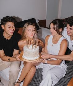 three people sitting on a bed with a cake in front of them and candles lit