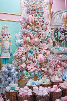 a pink christmas tree surrounded by baskets filled with cupcakes and other treats in front of a fireplace