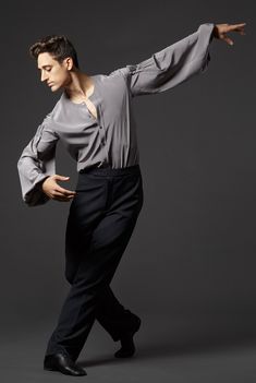 a man in grey shirt and black pants doing a dance move with his arms stretched out