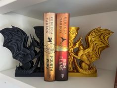 two books are sitting on a shelf next to a dragon figurine